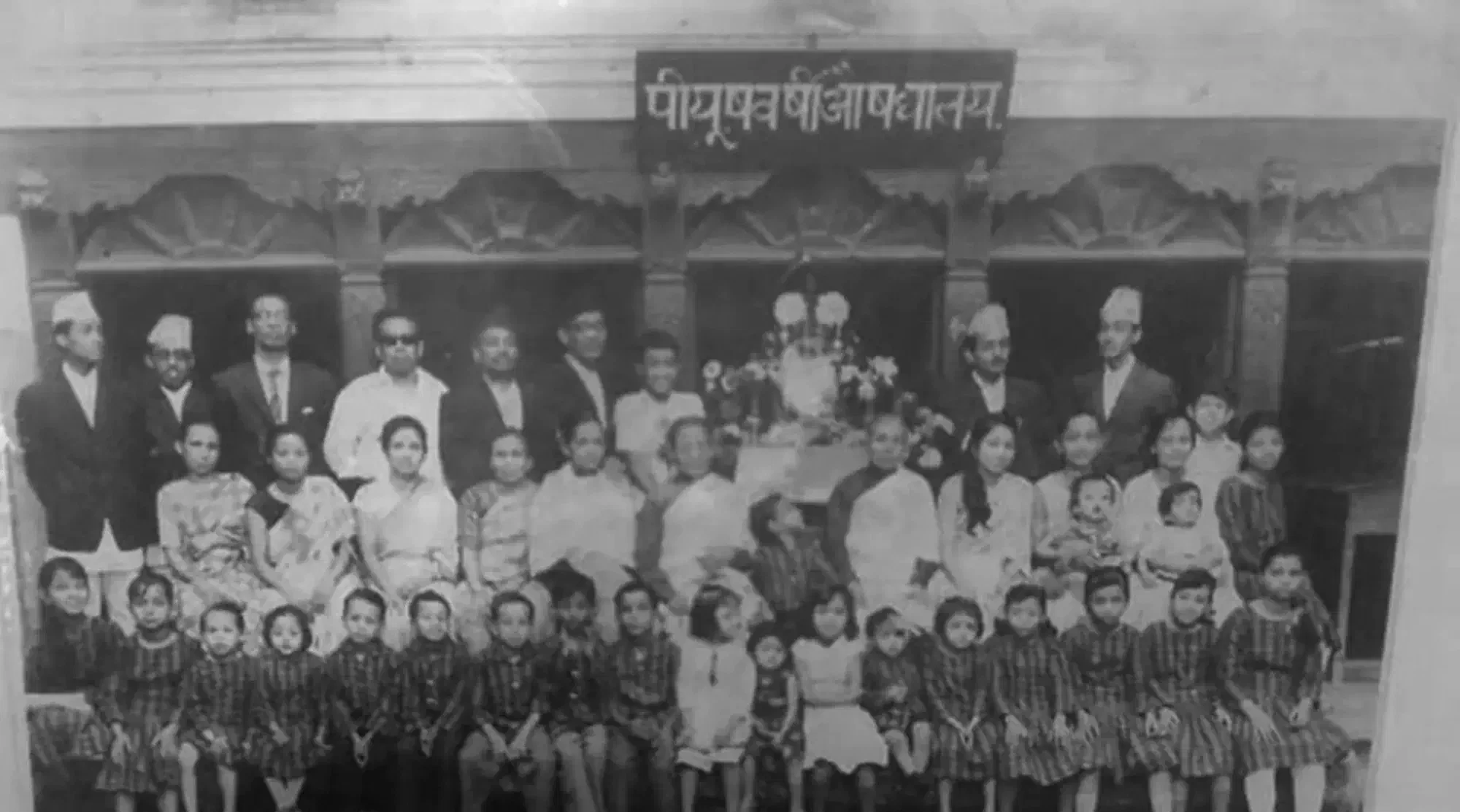 The Bajracharya family outside Piyushabarshi Aushadhalaya, beneath the clinic's signboard